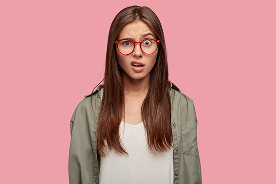 Indoor shot of indignant woman frowns face in displeasure, wears spectacles, shirt, models against pink background, doesnt like something dressed in casual shirt. Facial expressions concept.